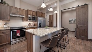 Eine moderne Küche mit Granit Arbeitsplatten, Edelstahlgeräten, Holzschränken und Pendelleuchten.