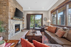 A living room with a stone fireplace, a large window, a sofa, and a television.