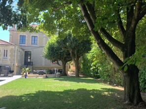 Un bâtiment doté d’une façade en pierre, de grandes fenêtres et d’une pelouse bien entretenue, avec un arbre au premier plan.
