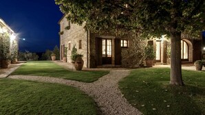 A stone building with a gravel path, large potted plants, and a tree in the foreground.