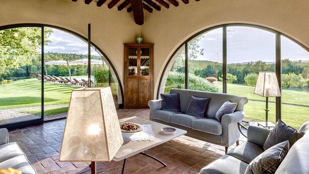 A spacious room with a large arched window, a sofa, a table with a bowl of fruit, and a cabinet.