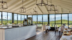 A spacious dining area with a large island, modern pendant lighting, and a scenic view through large windows.