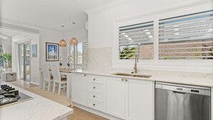 A modern kitchen with white cabinetry, a stainless steel dishwasher, and a window with blinds.