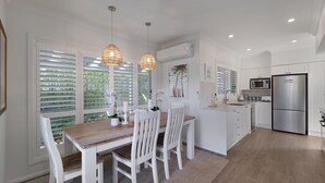 A modern kitchen with white cabinetry, a wooden dining table, white chairs, pendant lights, and a stainless steel refrigerator.