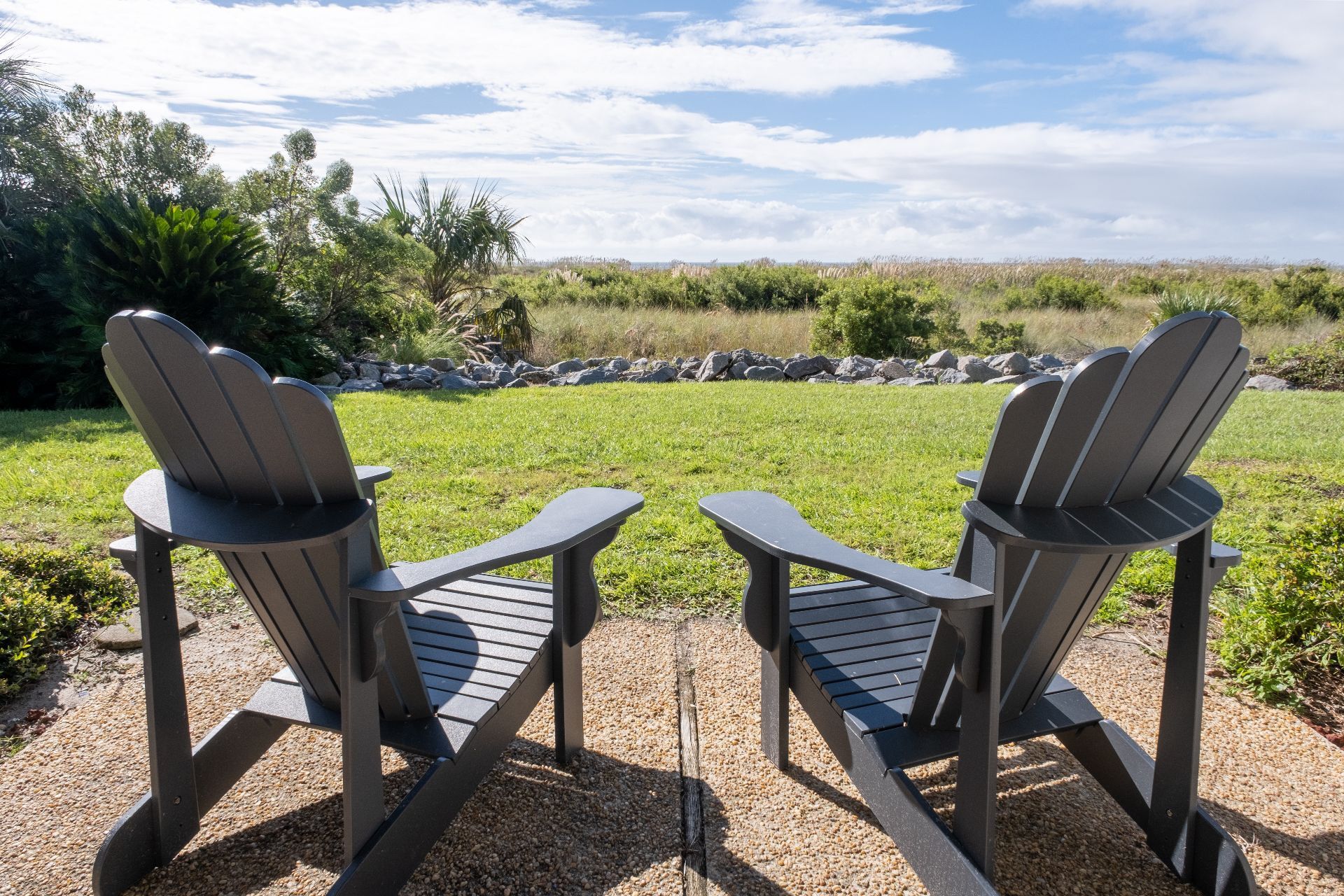 Twee Adirondack stoelen gericht op een grasveld, met een stenen muur en bomen op de achtergrond.