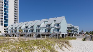 Un hotel frente a la playa con varios balcones, una playa de arena delante y un edificio alto al fondo.