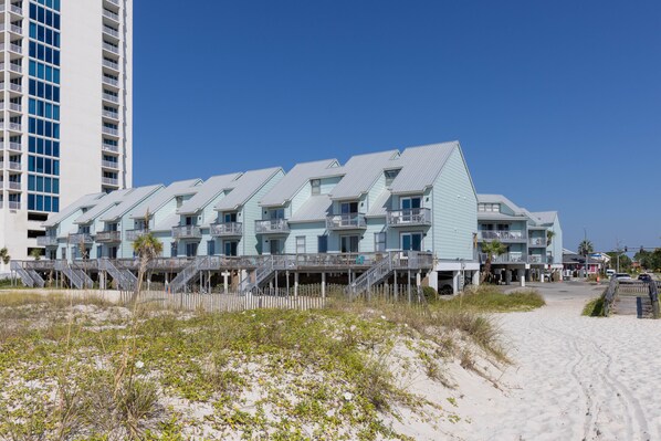 A beachfront hotel with multiple balconies, a sandy beach in front, and a tall building in the background.
