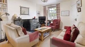 A cozy living room with a stone fireplace, a television, and a comfortable seating area with a red armchair and a sofa. - Oak Cottage, Chapel Stile (Chapel Stile)
