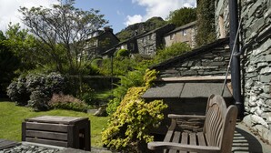 A stone building with a sloped roof, surrounded by lush greenery and a clear sky. - Oak Cottage, Chapel Stile (Chapel Stile)