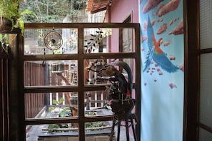 Una habitación con un ventanal grande dividido en varios paneles, una puerta de madera y un mural de pájaros en la pared.