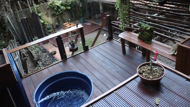 Une terrasse en bois avec un jacuzzi, des plantes en pot et une véranda donnant sur un jardin.
