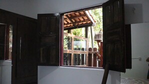 Une pièce dotée d’une grande fenêtre, de volets en bois et donnant sur un jardin.