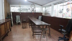 Un espace repas comprenant une longue table en bois, plusieurs chaises et un fauteuil de bureau noir.