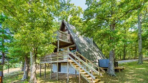 Une cabane en bois avec un escalier raide menant à une chambre à coucher située en mezzanine, le tout entouré d’arbres.