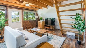Un intérieur de chalet chaleureux avec un canapé, une télévision, une échelle en bois et des plantes en pot.