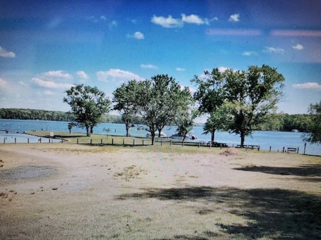 Un parque junto al lago con árboles, bancos y una vista despejada del agua.