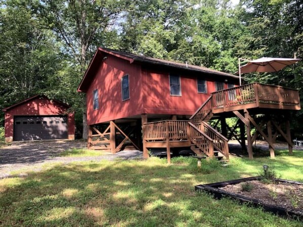 A red wooden cabin with a wooden deck and stairs leading to a balcony.
