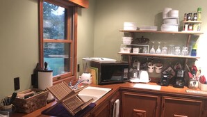Una cocina con armarios de madera, microondas, fregadero y ventana con vista a un espacio exterior verde.