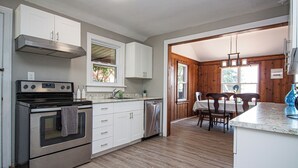 A modern kitchen with stainless steel appliances, white cabinetry, and a dining area with wooden chairs and a table.