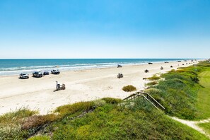 A beach with vehicles parked along the shore, a grassy area with a wooden structure, and a clear blue sky. - Beachfront w/ Rooftop Deck, Dune Walkover & Nearby to Jamaica Beach Amenities (Jamaica Beach)