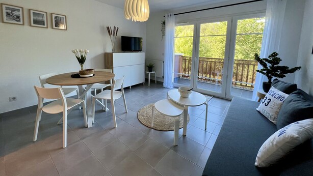 Una sala de estar moderna con comedor, un sofá, un televisor y un balcón con vistas a árboles.