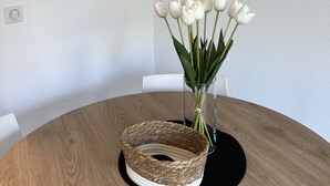 Una mesa redonda de madera con una cesta tejida y un jarrón de tulipanes blancos. Cuatro fotografías en blanco y negro, enmarcadas, están colgadas en la pared sobre la mesa.