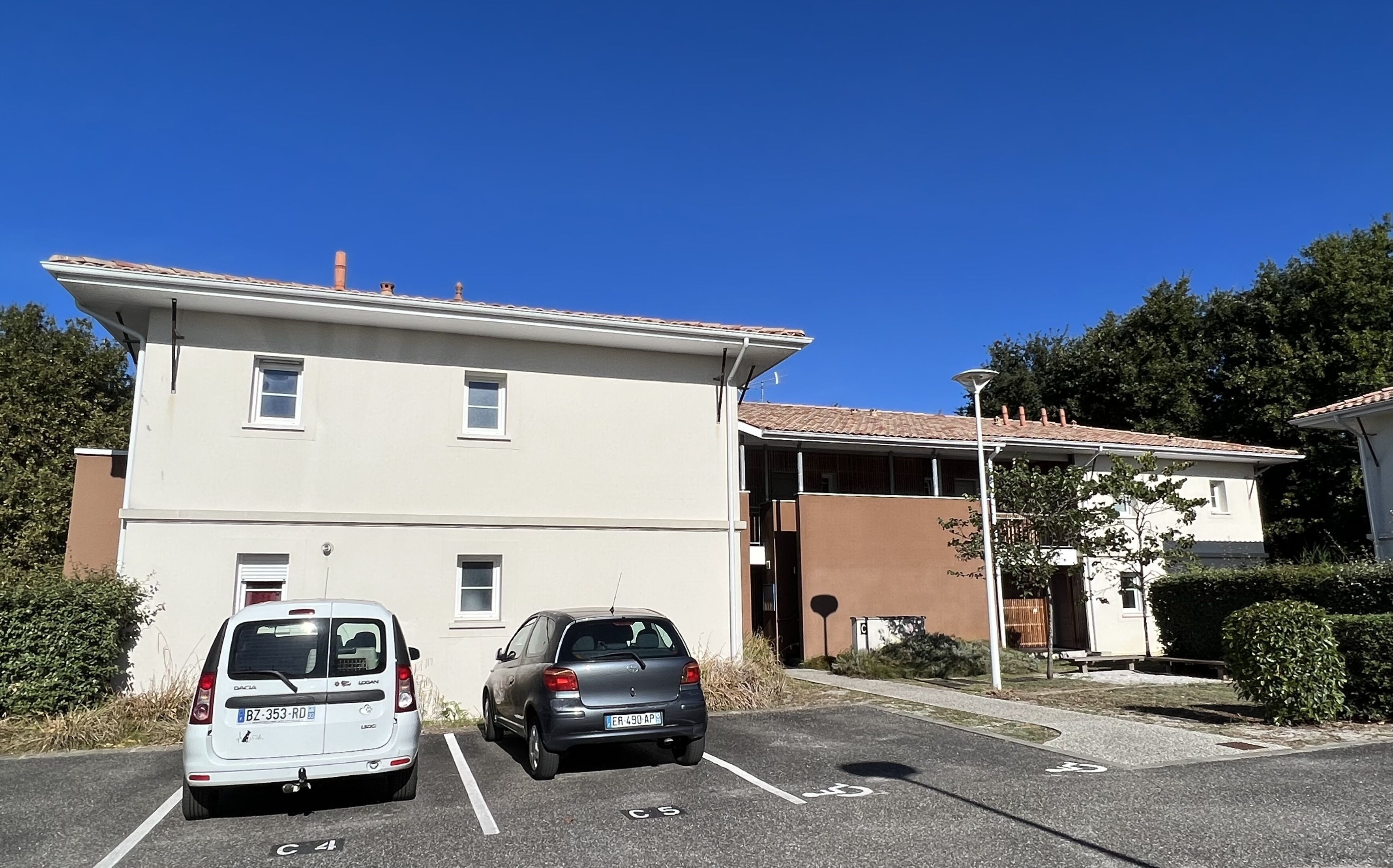 A parking lot with two cars, a building with a flat roof, and a clear blue sky.