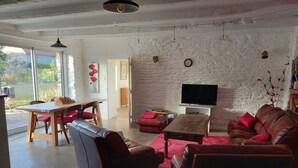 A living room with a stone wall, a wooden table, a leather sofa, and a television. - Single-storey house 100 m from the strikes (Courtils)