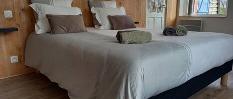 A neatly made bed with a wooden headboard, a window with curtains, and a view of the outside.