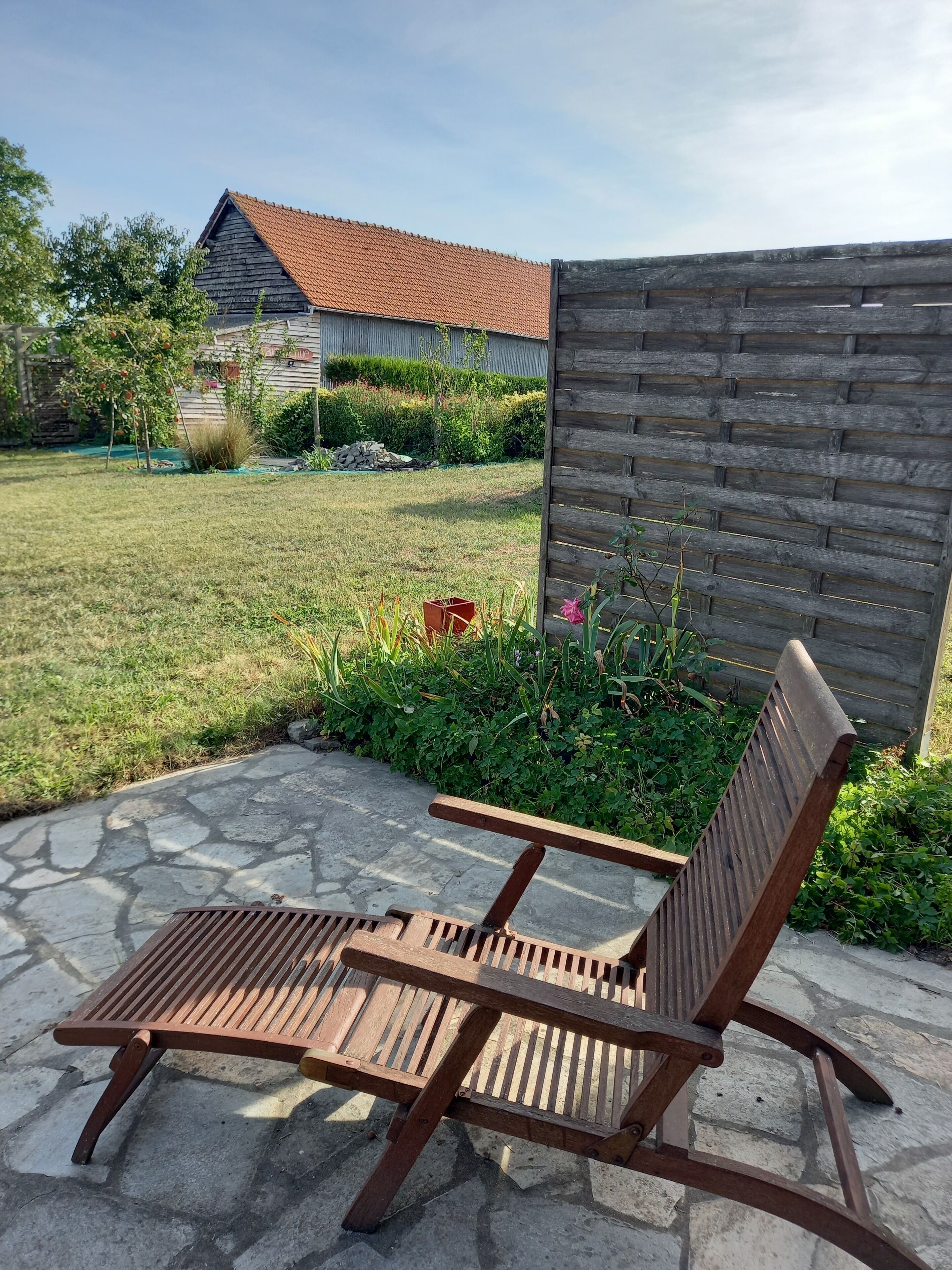 Un fauteuil de jardin en bois sur une terrasse en pierre, avec un jardin en arrière-plan.