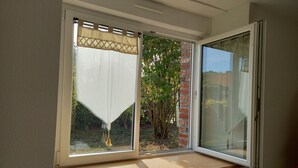 A room with a large window, a wooden bench, and a view of a garden with a brick wall and greenery. - Single-storey house 100 m from the strikes (Courtils)