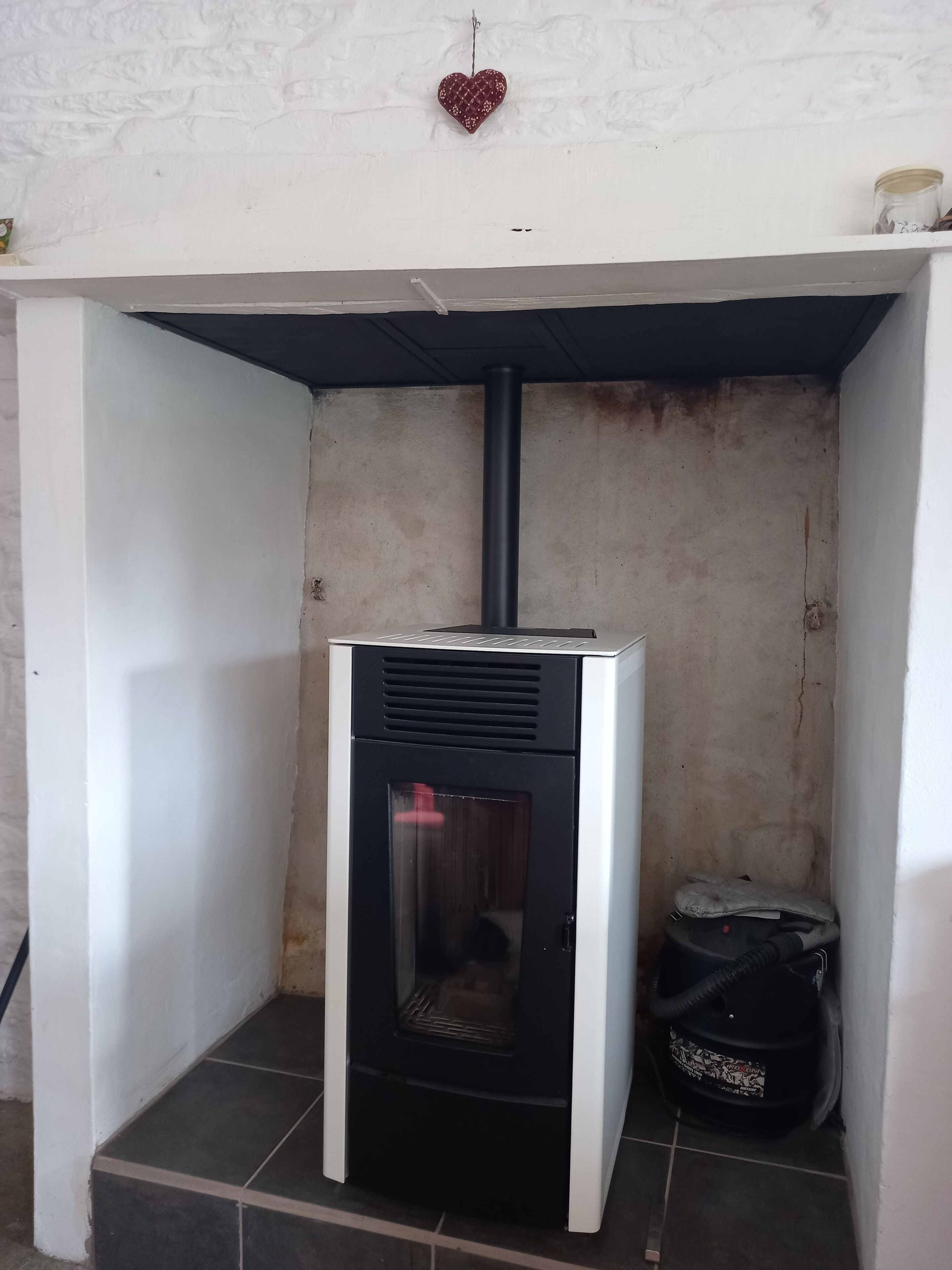 Une petite pièce équipée d’un chauffage électrique encastré, d’une petite étagère avec un pot et d’un décor en forme de cœur sur le mur.