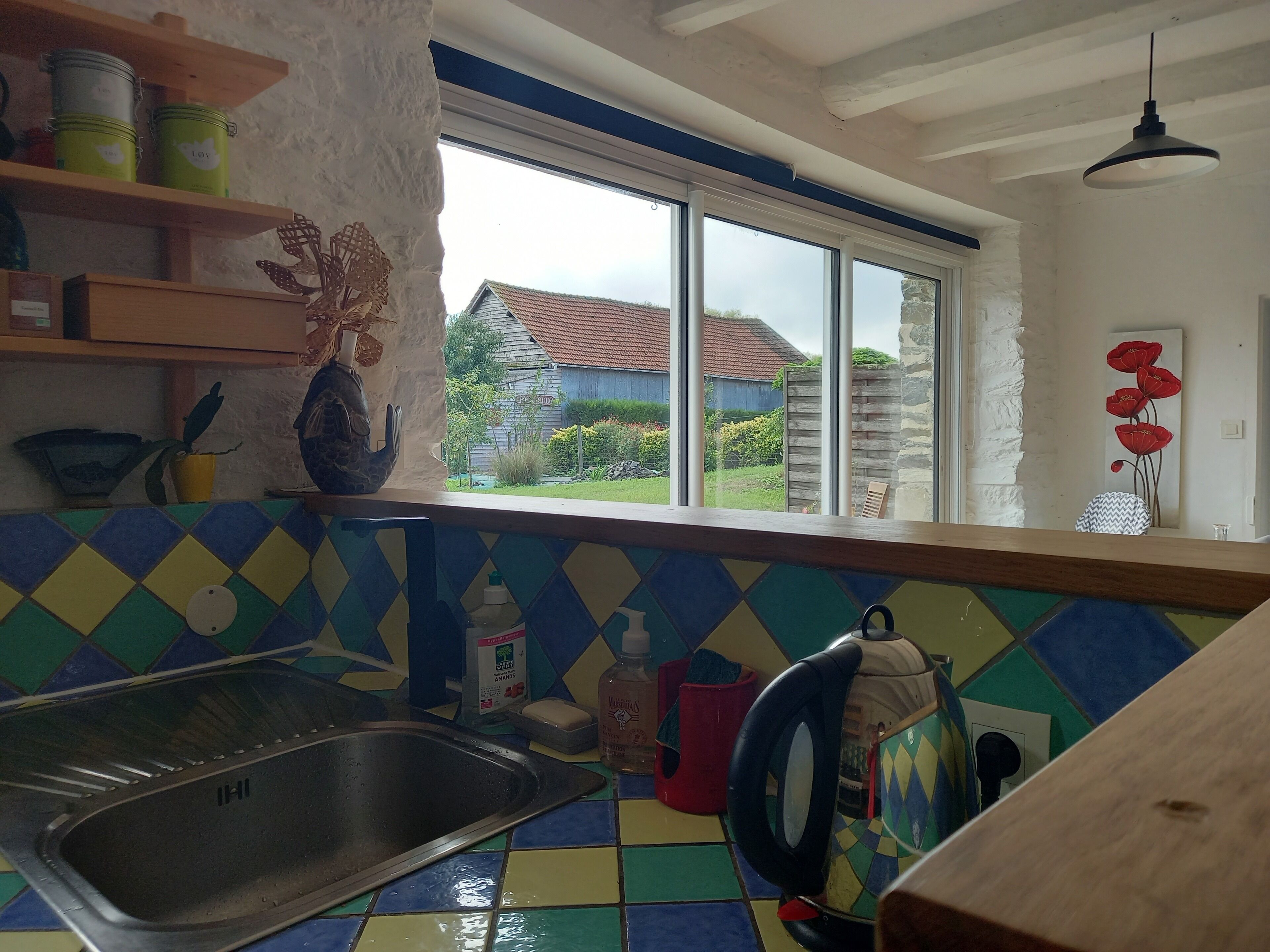 A kitchen with a large window, colorful tiles, a sink, and various kitchen items.