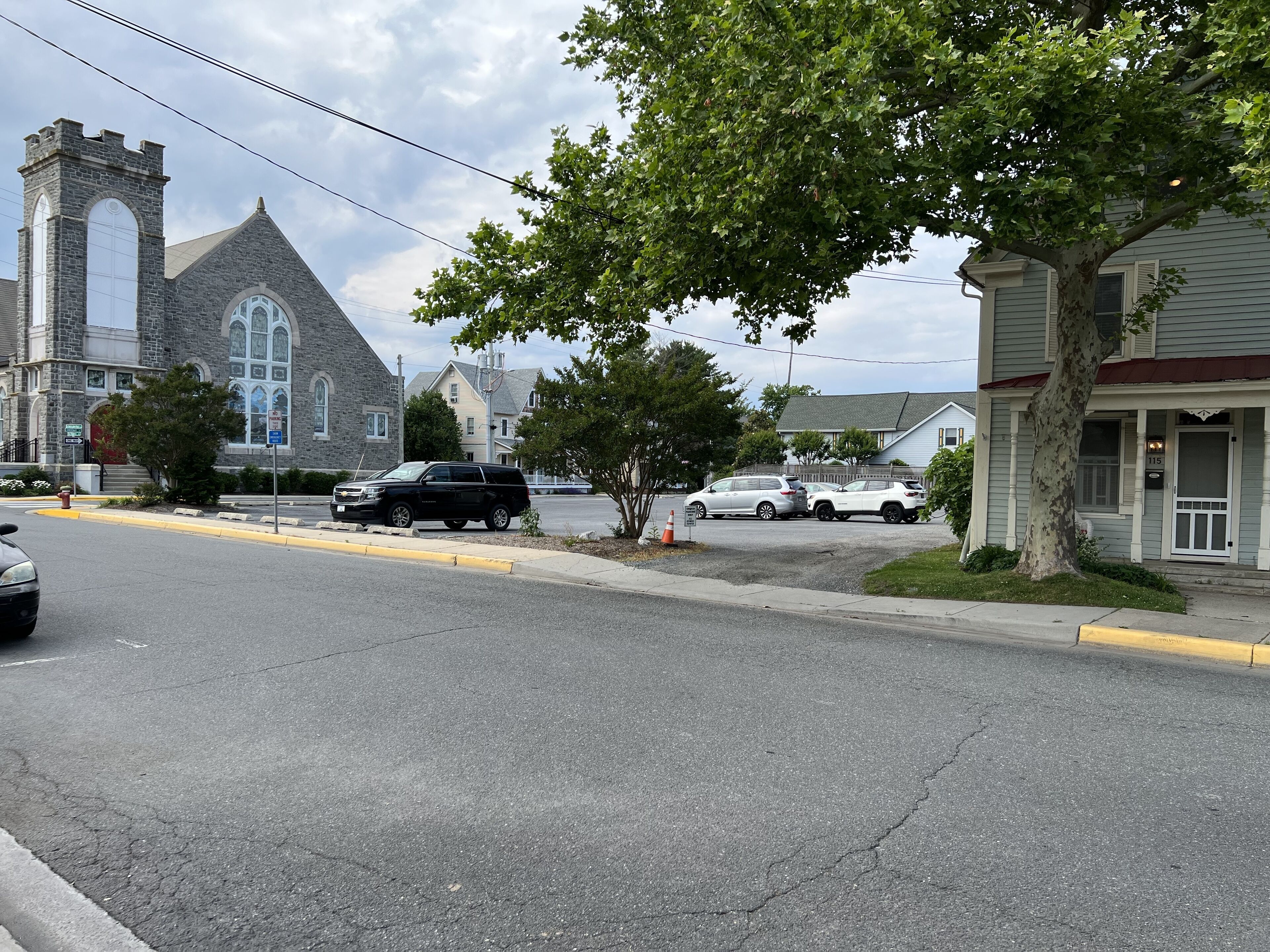 A street with a church, a black SUV, and a white SUV parked on the side.
