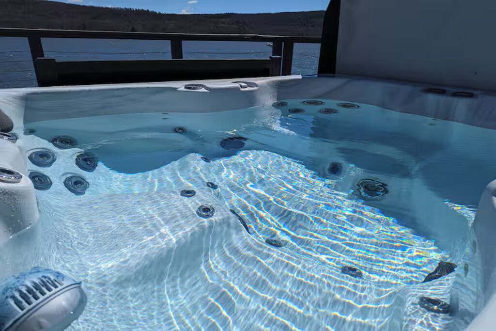 A hot tub with multiple jets, surrounded by a wooden deck, overlooking a body of water.