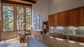 Une cuisine moderne avec des meubles en bois, des plans de travail en granit et de grandes fenêtres donnant sur une forêt.