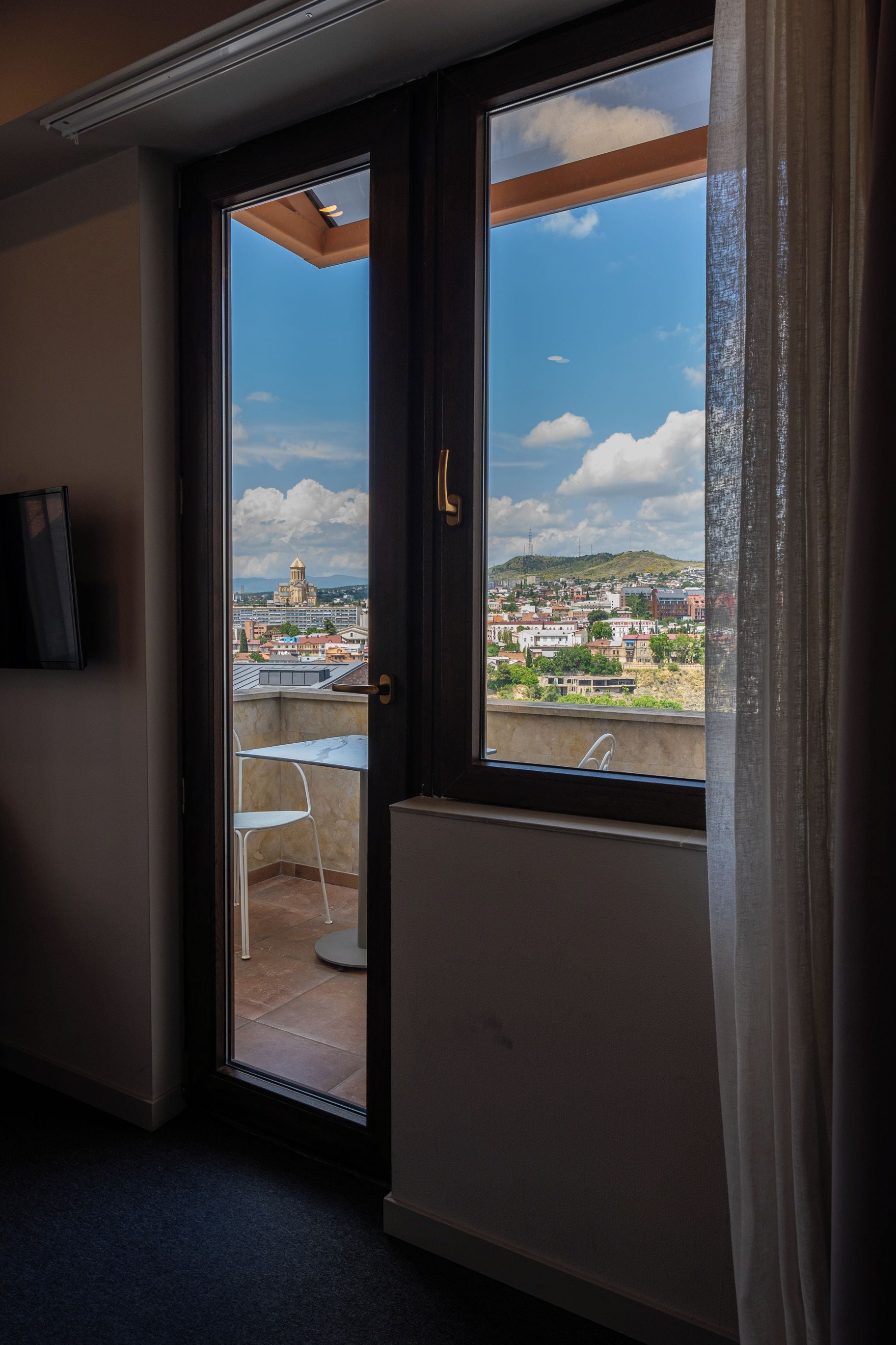 A room with a sliding glass door leading to an outdoor balcony with a view of a cityscape.