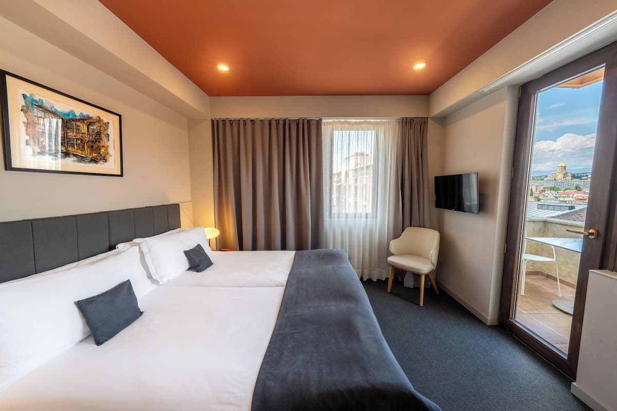 A hotel room with a bed, a chair, a TV, and a balcony with a view.