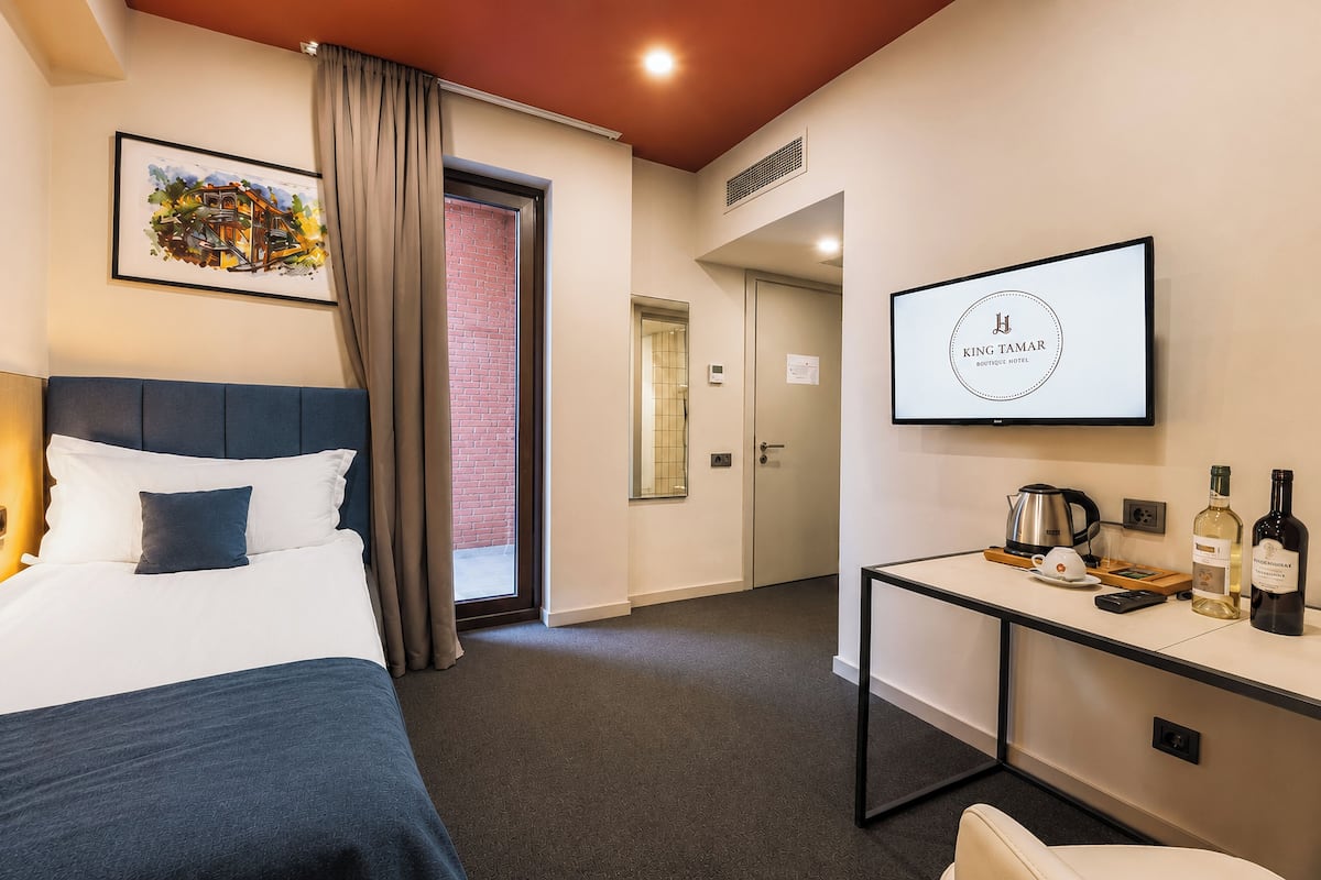 A hotel room with a bed, a desk with a TV, a kettle, and two bottles of wine.