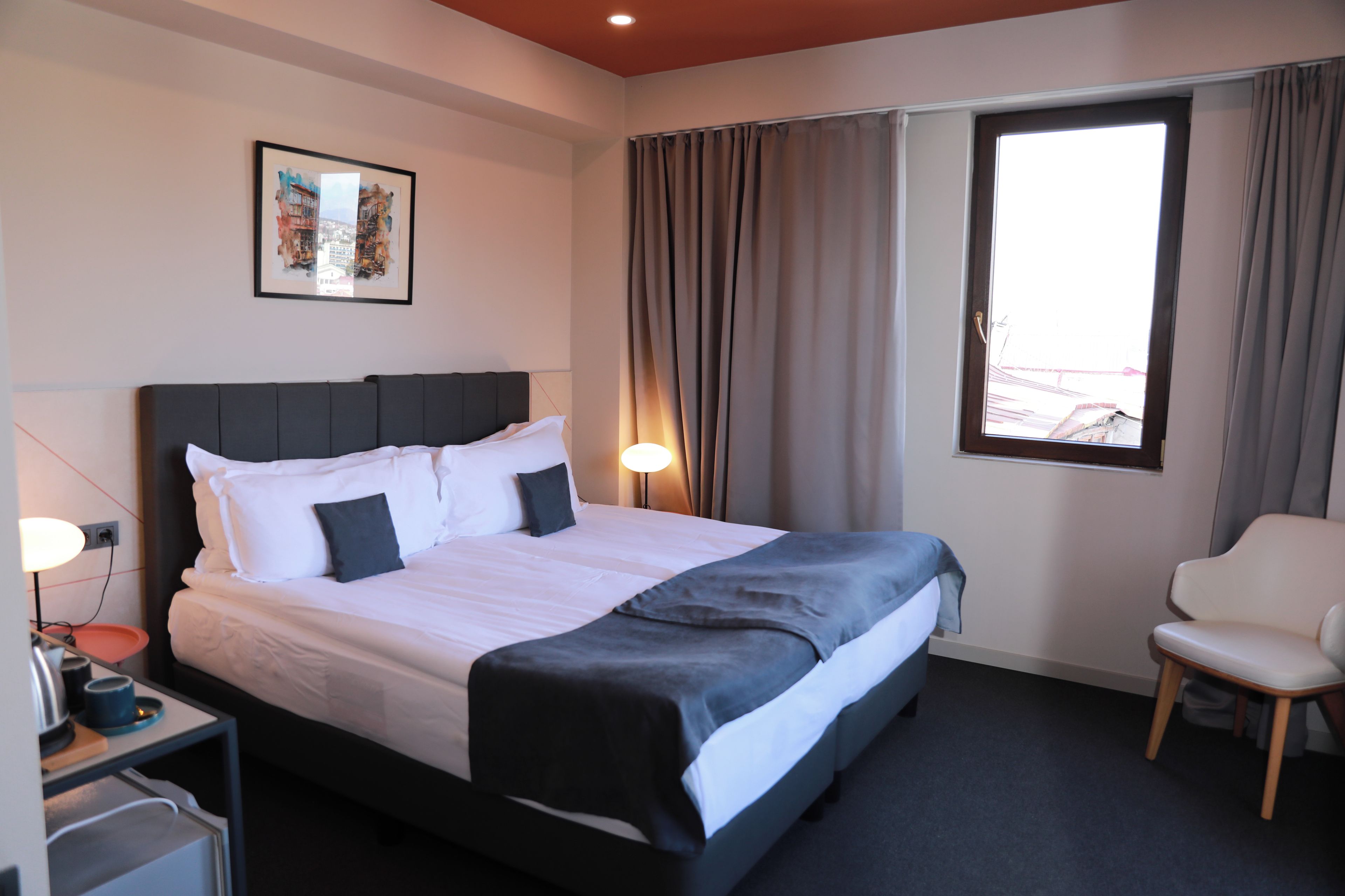 A hotel room with a bed, bedside table, lamp, chair, and a window with curtains.