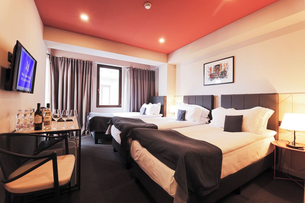 A hotel room with two beds, a desk with a chair, a TV, and a window with curtains.