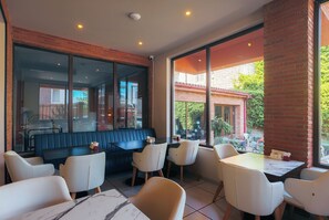 A restaurant interior with a brick wall, large windows, and a mix of seating arrangements including booths and tables. - KING TAMAR HOTEL By LUXURIA HOTELS (Tbilisi)