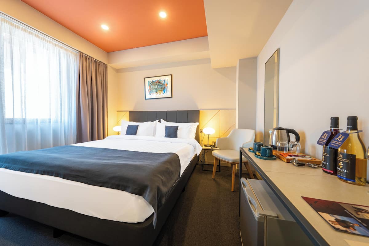 A hotel room with a bed, bedside table, lamp, chair, and a minibar.