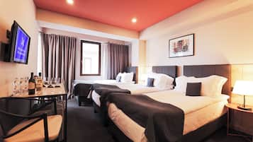 A hotel room with two beds, a desk with a chair, a TV, and a window with curtains.