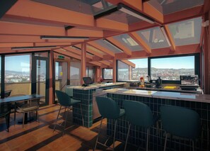 Zona de bar moderna con techo alto, ventanas amplias y vistas a un paisaje urbano.