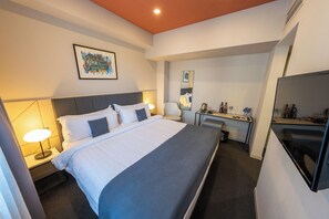 A hotel room with a bed, bedside table, lamp, desk with a mirror, and a television. - KING TAMAR HOTEL By LUXURIA HOTELS (Tbilisi)
