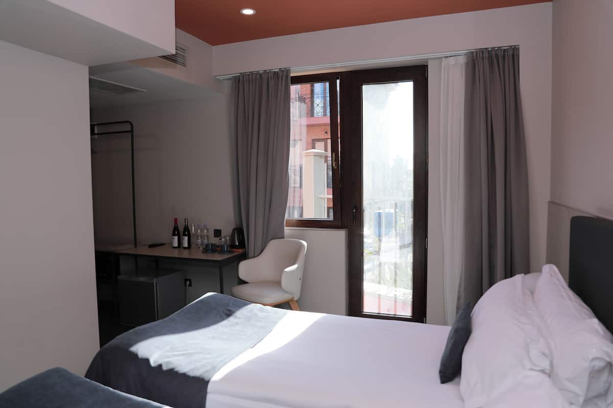 A hotel room with a bed, a desk, a chair, and a view of the city through a window.