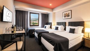 A hotel room with two beds, a desk with a chair, a TV, and a window with curtains. - KING TAMAR HOTEL By LUXURIA HOTELS (Tbilisi)