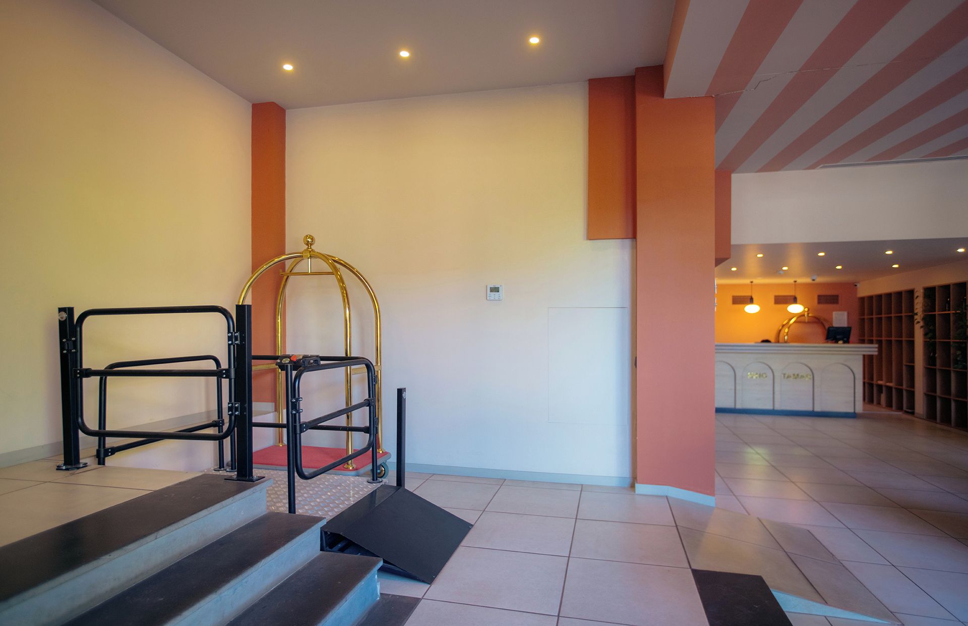Een hotelhal met een trap, een lif voor rolstoelen en een receptie.
