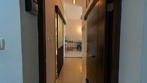 A narrow hallway with a door on the right, a light fixture above, and a kitchen area visible through an open door at the end. - Hotel comfort in a prestigious residence (Chéraga)